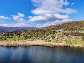 Un village au bord d’un lac, avec des maisons construites sur une colline, un ciel dégagé et des montagnes en arrière-plan.