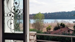 Vista desde una ventana con reja ornamental, sobre un lago y una ladera boscosa.