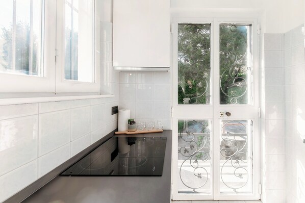 A modern kitchen with white tiles, a black stove, and a glass door with decorative ironwork.