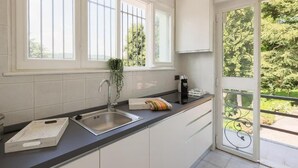 Una cocina con armarios blancos, encimera negra, pileta de acero inoxidable y ventana con vista a follaje.