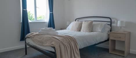 Une chambre avec un lit simple, une table de chevet avec une lampe et une fenêtre avec des rideaux.