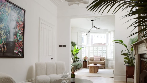 Ein modernes Wohnzimmer mit einer Couch, einem Couchtisch mit Flasche und Gläsern, einem Kamin und einem großen Gemälde an der Wand.