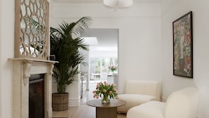 Ein modernes Wohnzimmer mit Kamin, einer großen Kühlpflanze, einem runden Couchtisch mit Blumen und einem weißen Sofa.