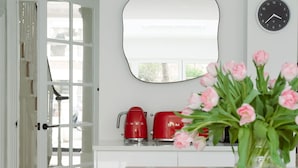 Eine moderne Küche mit weißen Schränken, einer roten Kaffeemaschine und einem Strauß rosa Blumen auf der Arbeitsfläche.