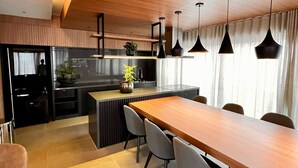 A modern kitchen with a wooden island, black pendant lights, and a dining area with a long table and chairs. - Itaim Retreat Luxury 1 Bedroom in Itaim (São Paulo)