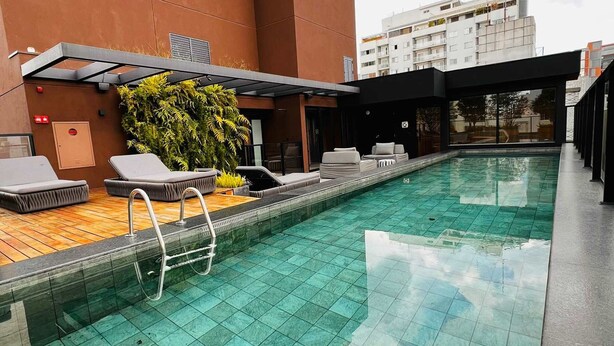 A rooftop swimming pool with clear blue water, surrounded by lounge chairs and a covered seating area. - Itaim Retreat Luxury 1 Bedroom in Itaim (São Paulo)