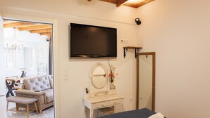 Un dormitorio con cama, televisor, tocador con espejo y puerta que da a una sala de estar.