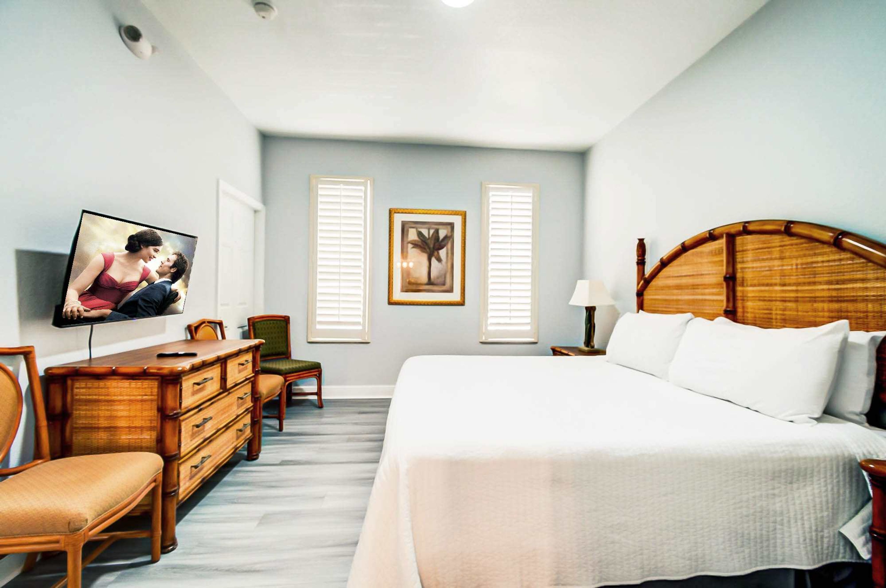 A bedroom with a large bed, a wooden dresser, a television, and two framed pictures on the wall.