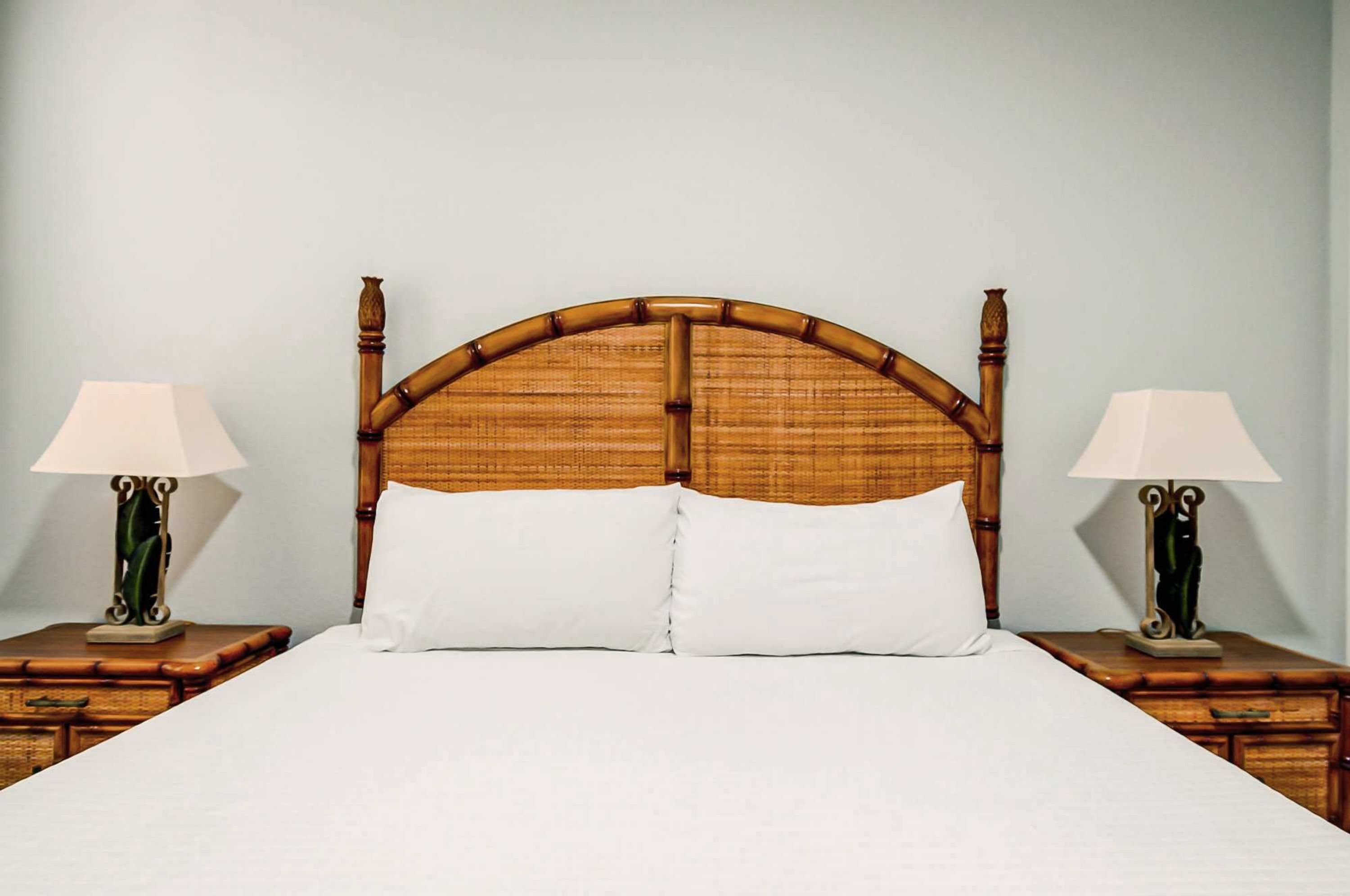 Una cama con cabecera de madera, dos mesitas de noche con lámparas y una colcha blanca.