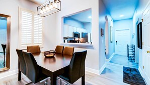 A modern dining area with a dark wooden table and leather chairs, a pendant light, and a view into a kitchen with white cabinets. - 3602 Fantastic 4BD Townhouse For Family Vacation (Davenport)