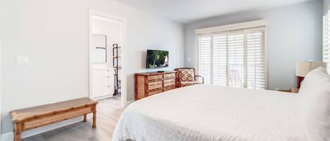 Un dormitorio con una cama grande, un banco de madera, un aparador, un televisor y una ventana con persianas.