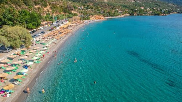 Ein Küstenstrand mit klarem türkisblauem Wasser, Sonnenschirmen und badenden Personen.