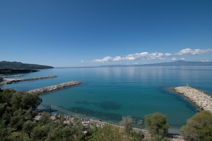 A coastal view with clear blue water, rocky breakwaters, and distant mountains.
