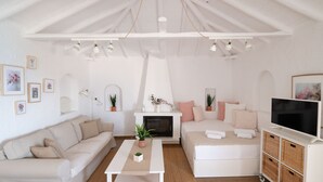 Ein gemütliches Wohnzimmer mit einem weißen Sofa, einem weißen Sessel, einem Kamin und einem Fernseher auf einer weißen Kommode.
