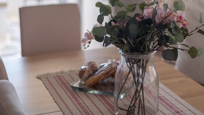Ein Essbereich mit einem Tisch für zwei Personen, einer Blumenvase und Blick auf das Meer durch das Fenster.