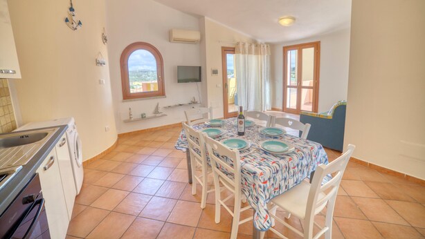 A dining area with a table set for four, a washing machine, and a TV on the wall. - La Teresina di Gallura: Crystal clear sea (Santa Teresa)