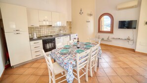 A compact kitchen with white cabinets, a tiled backsplash, a dining table set with blue plates, and a TV mounted on the wall. - La Teresina di Gallura: Crystal clear sea (Santa Teresa)