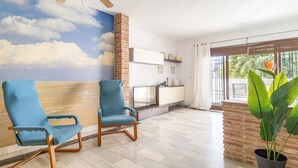 Ein Wohnzimmer mit zwei blauen Sesseln, einem Fernseher, einer Ziegelwand und einem großen Fenster mit Blick auf Grünflächen.