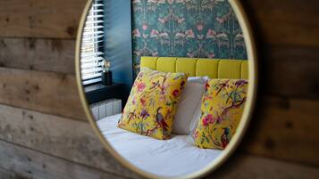 Una cama con almohadones florales, cabecera amarilla y papel tapiz con motivos naturales.