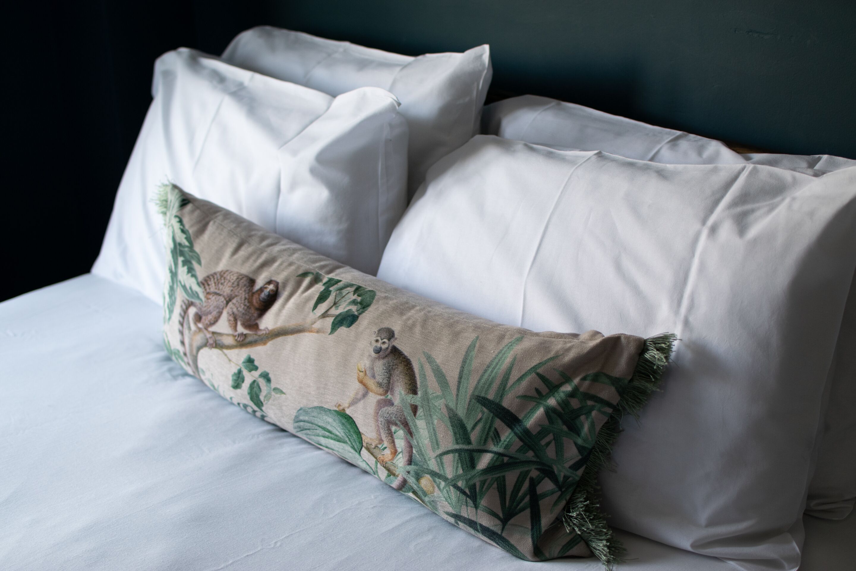Un lit avec du linge de lit blanc et un coussin décoratif orné d’un motif inspiré de la nature.