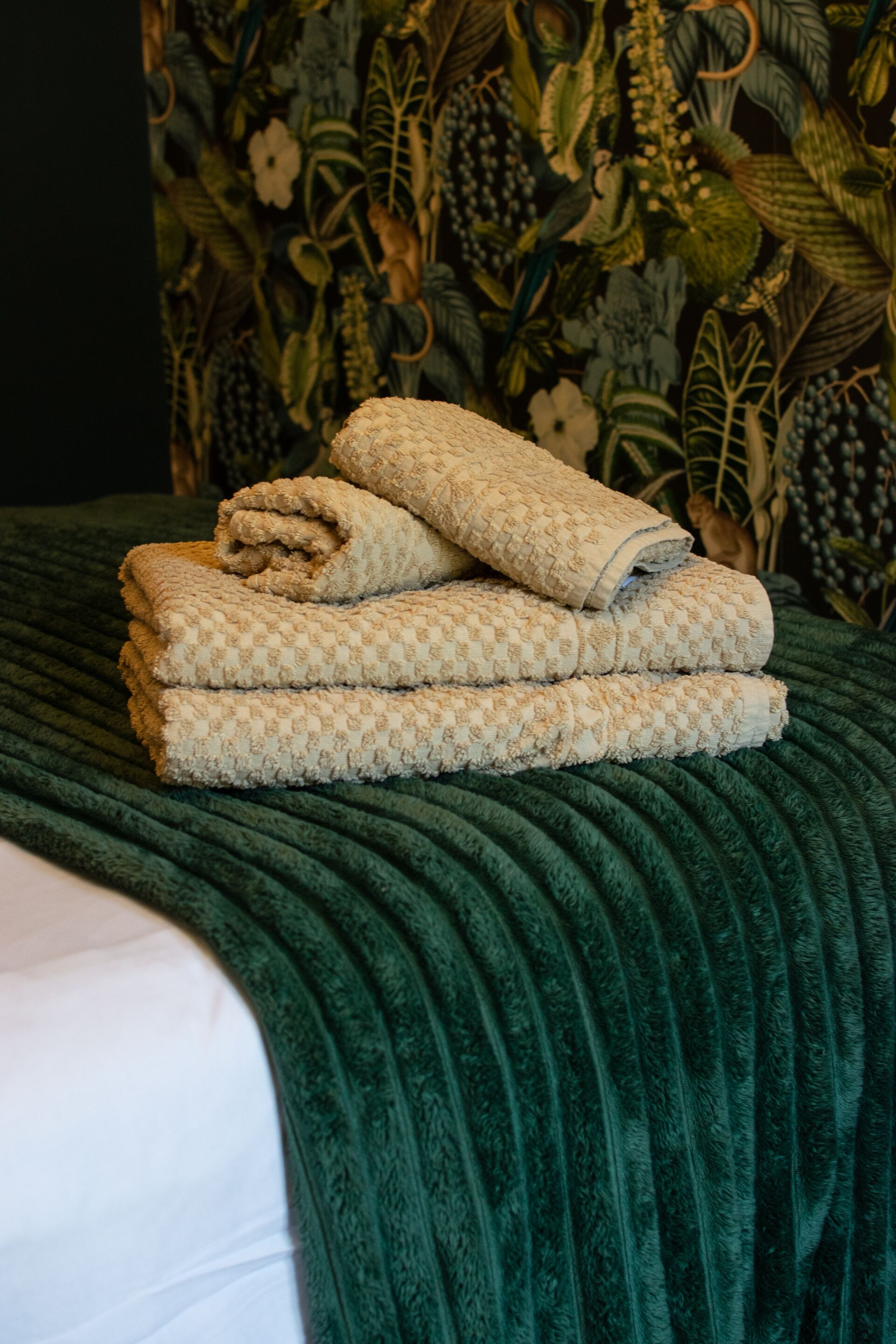 A bed with a green textured blanket and a patterned pillow.