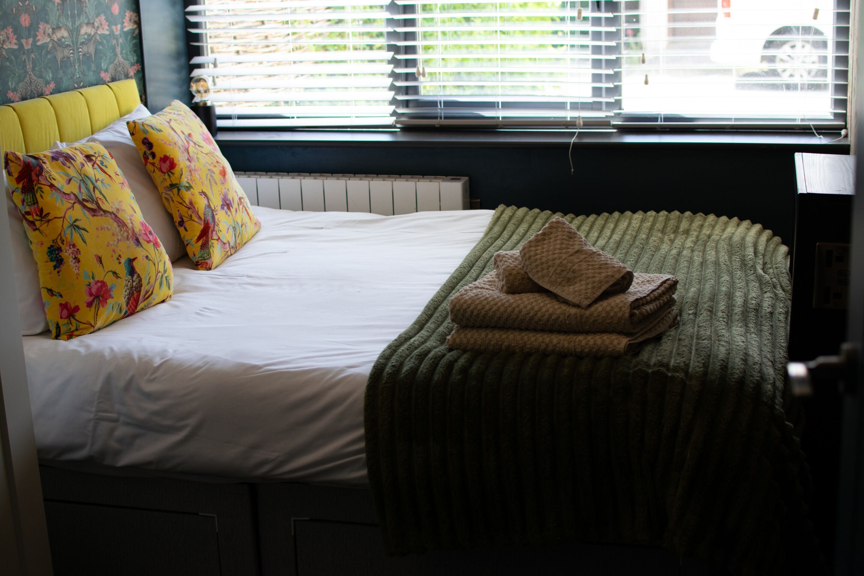 A bed with floral pillows, a green blanket, and a radiator.