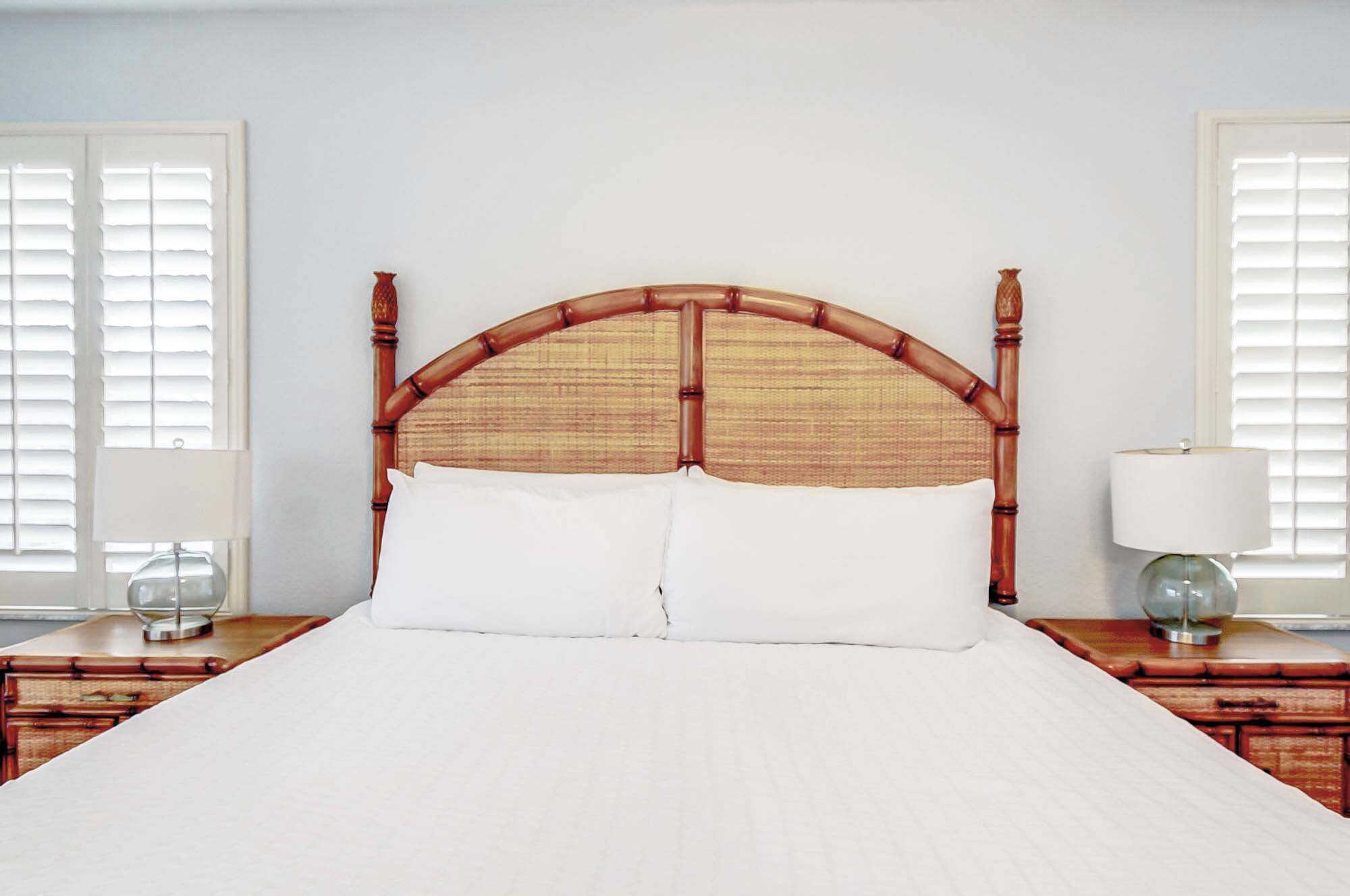 A bed with a bamboo headboard, white bedding, and two bedside tables with lamps.