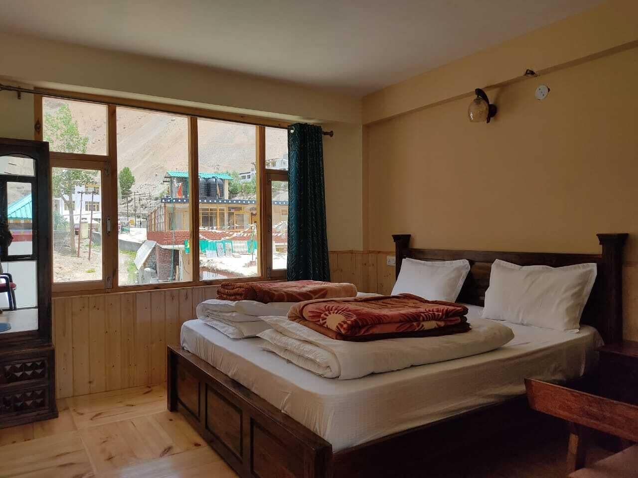 A bedroom with a wooden bed, a window with a view of the outside, and a small table with a chair.