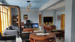 A living room with a fireplace, a television, and a dining area with a round table. - The old monk (Spiti)