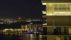 Ein modernes Gebäude mit einem großen Riesenrad im Hintergrund, Blick auf das Wasser und eine nächtliche Skyline.