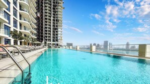 Blick vom Pool auf ein Hochhaus, strahlend blauer Himmel und eine entfernte Stadtlandschaft.