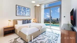 Ein modernes Hotelzimmer mit einem großen Bett, Blick auf die Stadt, einem Fernseher und einem gerahmten Kunstwerk an der Wand.