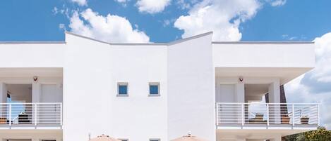 A modern building with two balconies, each with a white railing and a door.