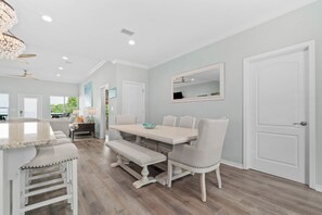 A dining area with a white table, chairs, and a bench. There is a ceiling fan, recessed lighting, and a door with a mirror. - Bayfront home with excellent view of the D.I. Bridge (Dauphin Island)