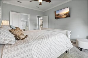 A bedroom with a bed, a nightstand, a chair, a ceiling fan, a painting, and a view of a dock and sunset. - Bayfront home with excellent view of the D.I. Bridge (Dauphin Island)