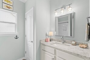 A bathroom with a white vanity, a mirror, a sink, and a towel rack. - Bayfront home with excellent view of the D.I. Bridge (Dauphin Island)
