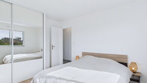 A modern bedroom with a large bed, a wardrobe with a mirror, and a bedside lamp. - Modern house for 8 at 400m from the beach (Plouguerneau)