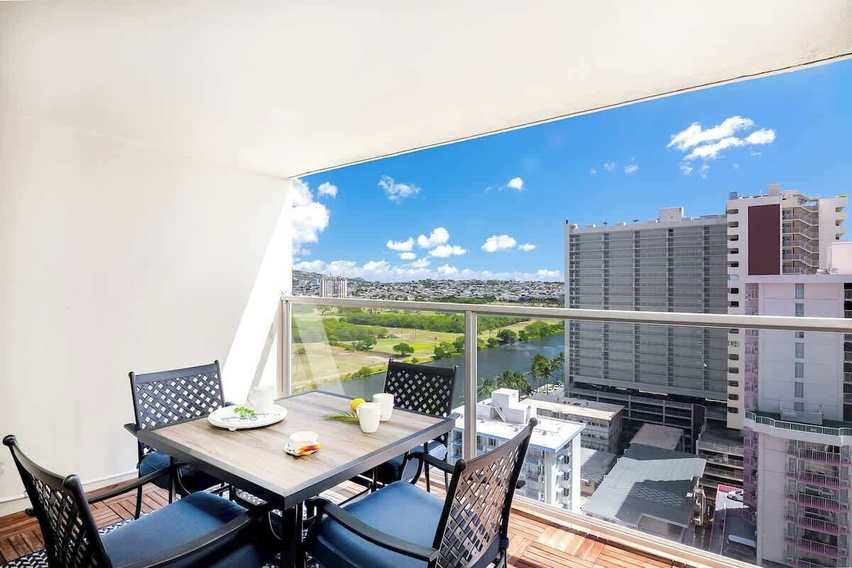 Un balcón con mesa y sillas, vista a un paisaje urbano y un río.