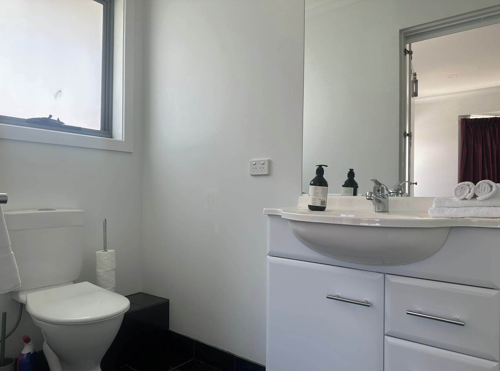 Een badkamer met toilet, wastafel, spiegel en handdoekhouder.