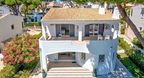 A white villa with a tiled roof, a covered patio with chairs, and a small garden with pink flowers. - Old Village Area, Your Perfect Vilamoura Getaway, Private Pool, AC & Wifi (Loulé)