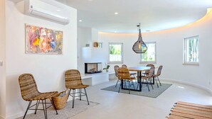 Une salle à manger moderne avec une table ronde et des chaises en osier, une cheminée et un grand tableau abstrait accroché au mur.