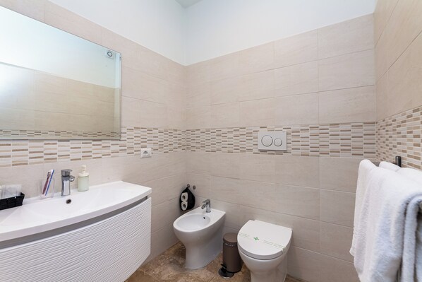 A modern bathroom with a large mirror, a freestanding bathtub, a bidet, and a toilet. - Vatican Luxury Apartment (Rome)