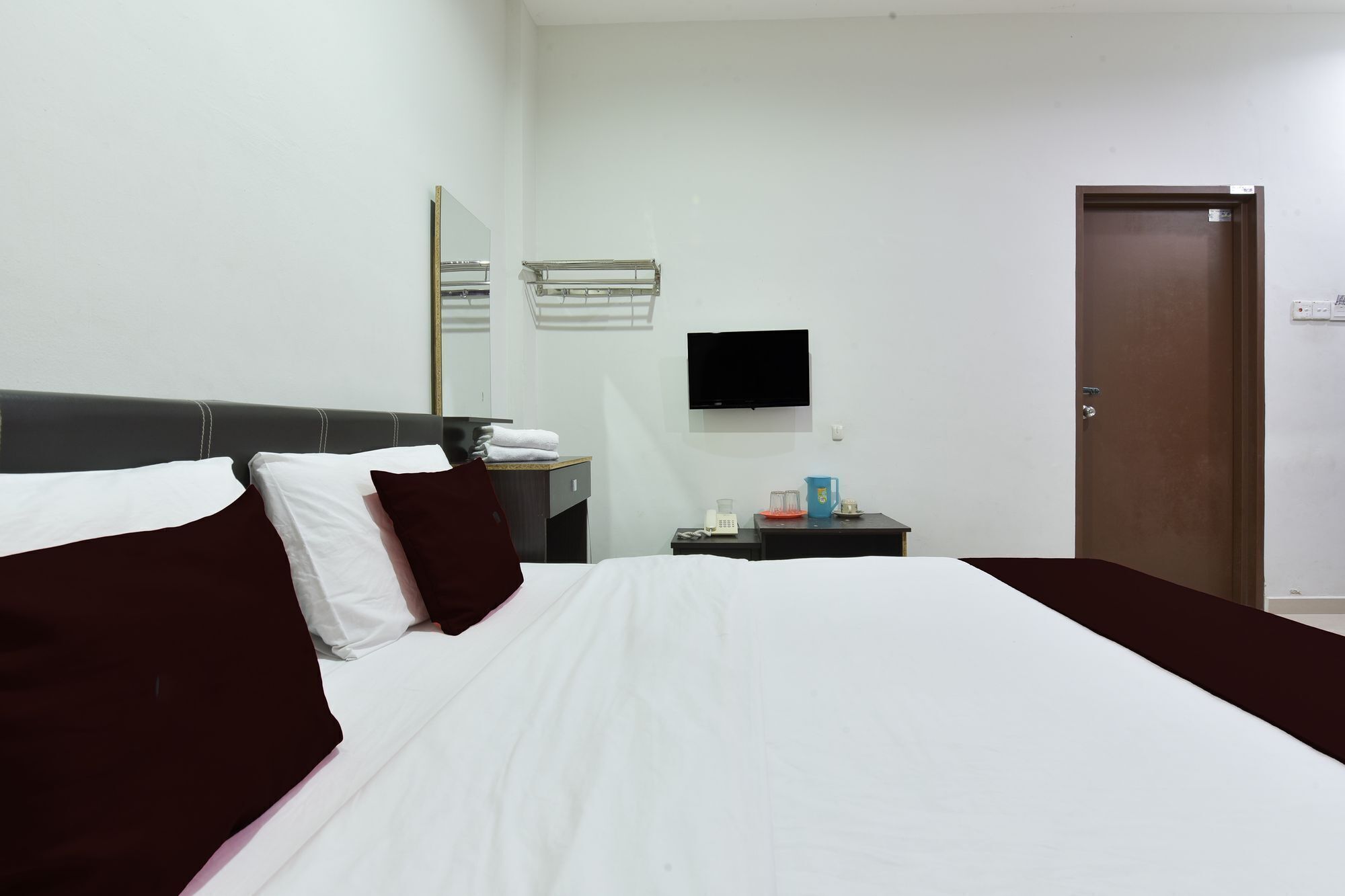 Una habitación de hotel con cama, mesita de noche, televisión, espejo y puerta.