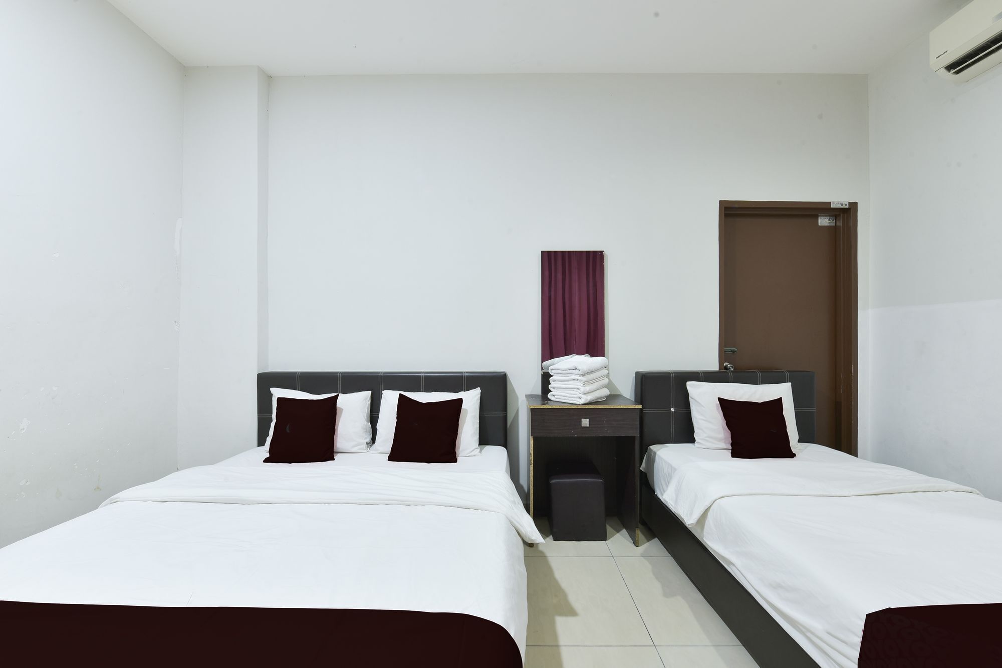 A hotel room with two single beds, a small desk with a chair, a wardrobe, and a door.