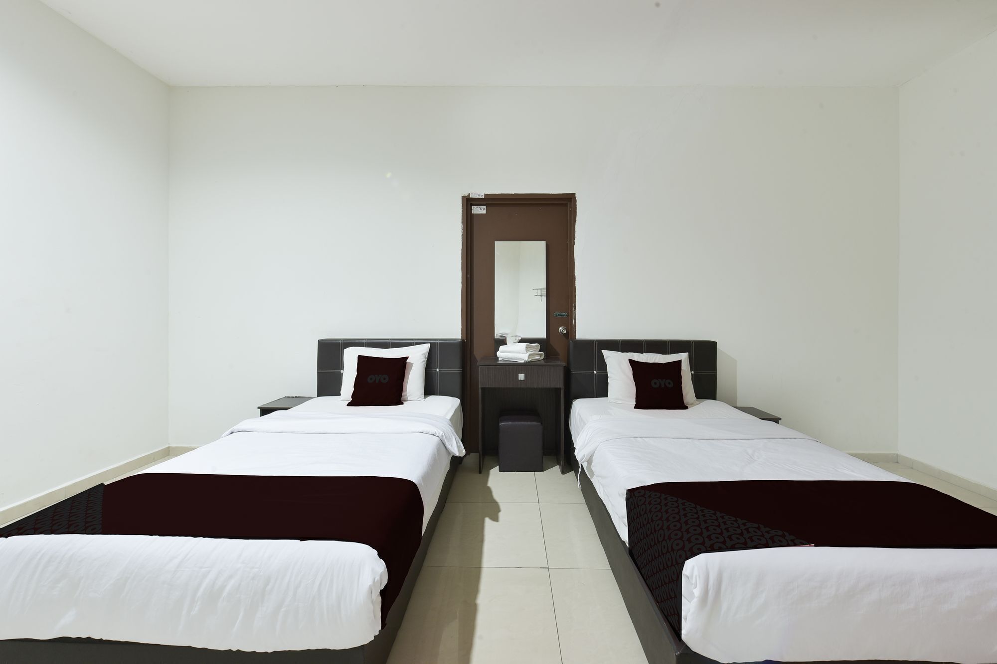 Una habitación de hotel con dos camas individuales, una mesita de noche pequeña, un espejo y una puerta.