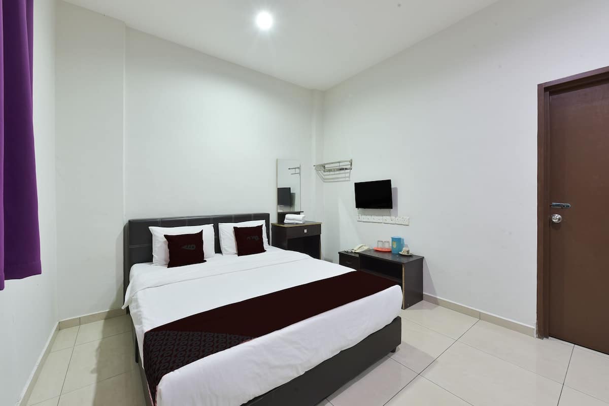 A hotel room with a bed, a bedside table, a TV, and a door.