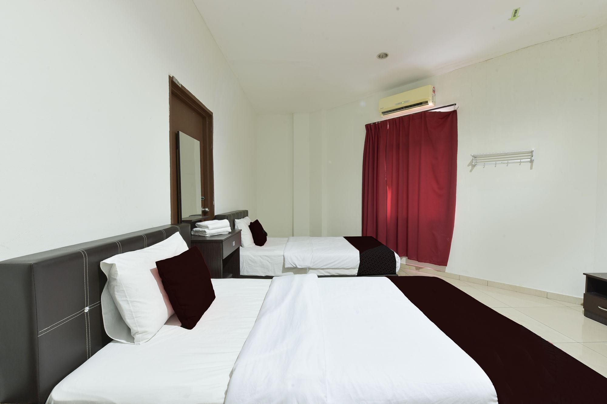 A hotel room with two beds, a large mirror, a red curtain, and a wall-mounted air conditioning unit.