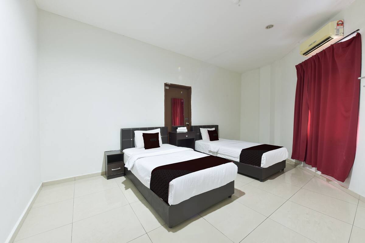 A hotel room with two beds, a nightstand, a mirror, and a red curtain.