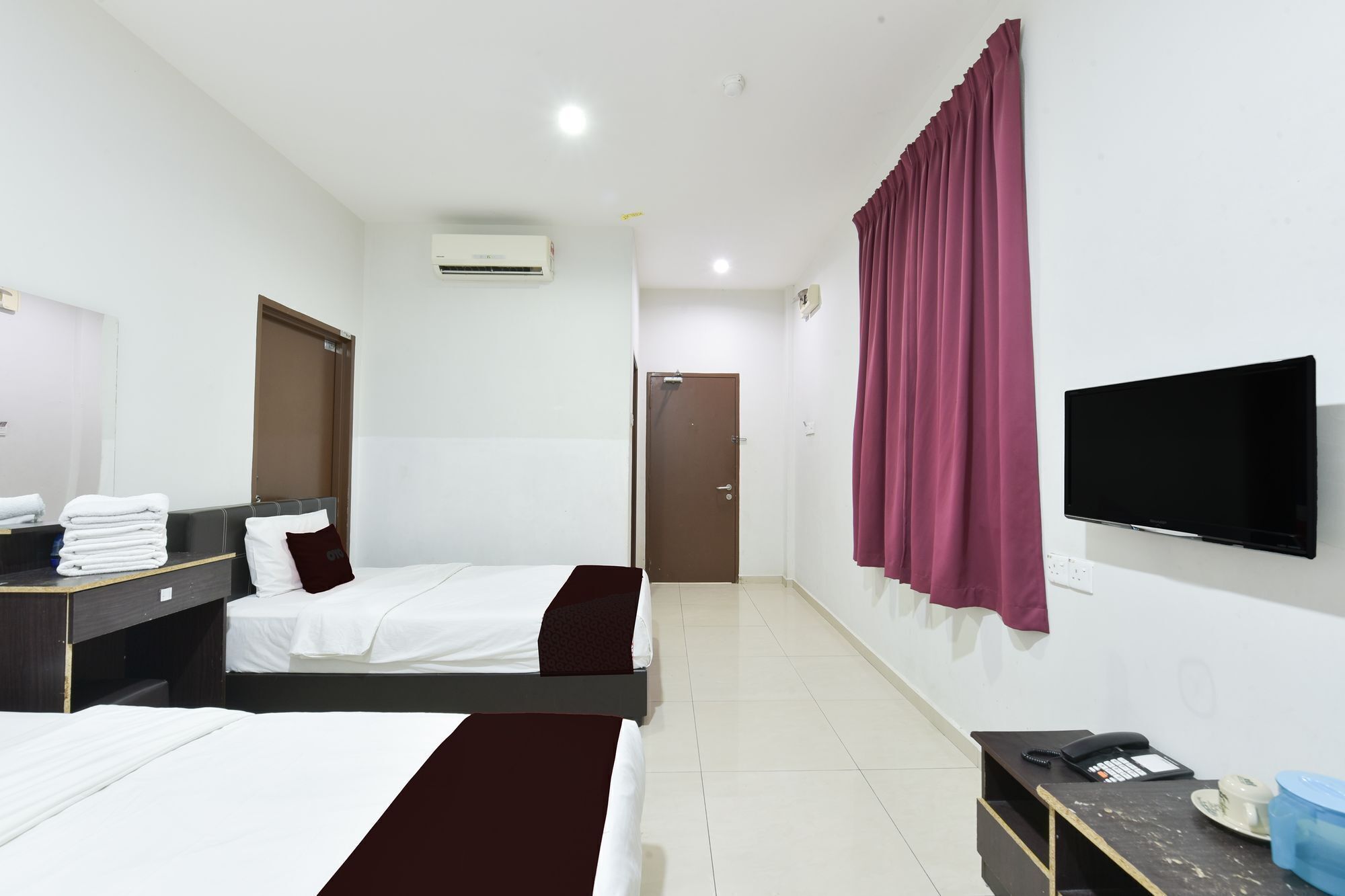 A hotel room with two beds, a TV, a desk with a phone, and a mirror.