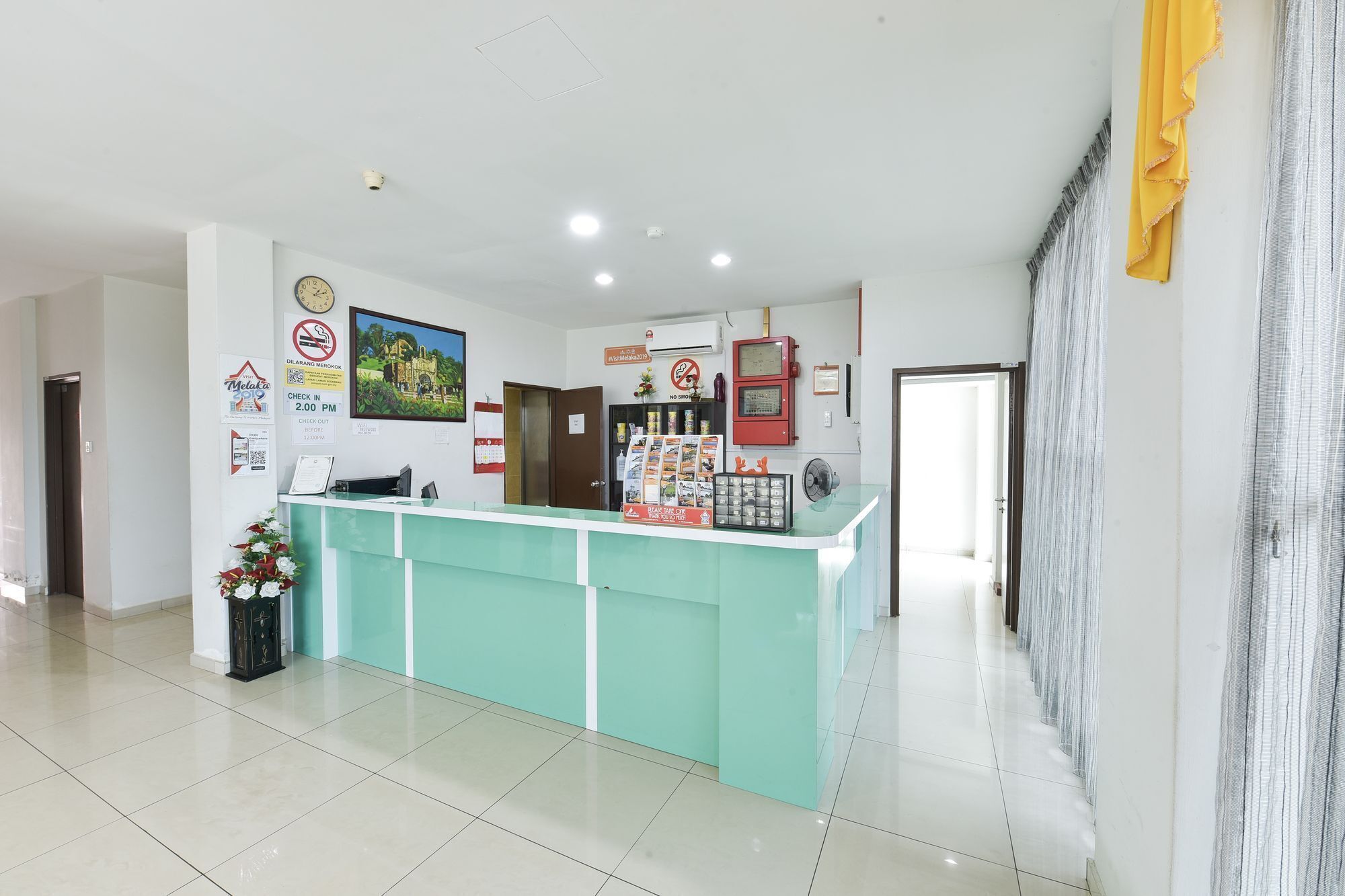 Uma área de recepção de hotel com um balcão em tons de verde-água, um relógio e diversos cartazes informativos.